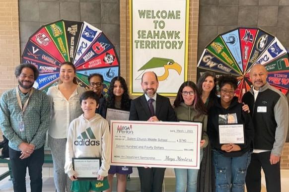 A group of students and school faculty pose with an oversized check from MEGA Mentors.