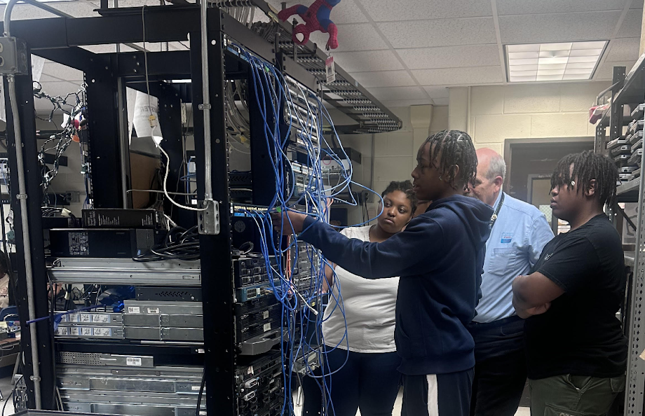 Four people look at a rack of computer equipment.